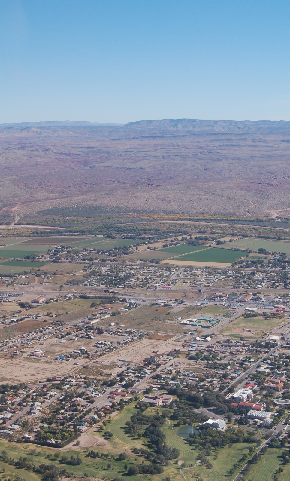 上空から見たニューメキシコ州ソコロの市街地、リオ・グランデ沿いの農地、周囲の乾燥した丘陵。